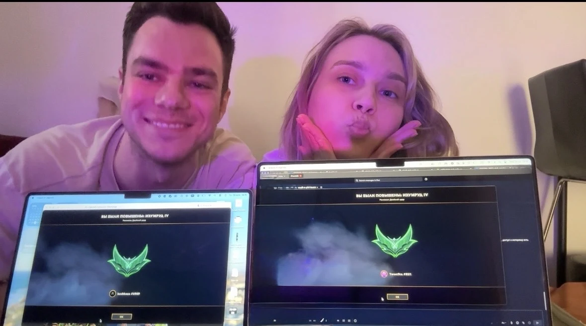 A couple smiling behind two MacBooks showing TFT screens.